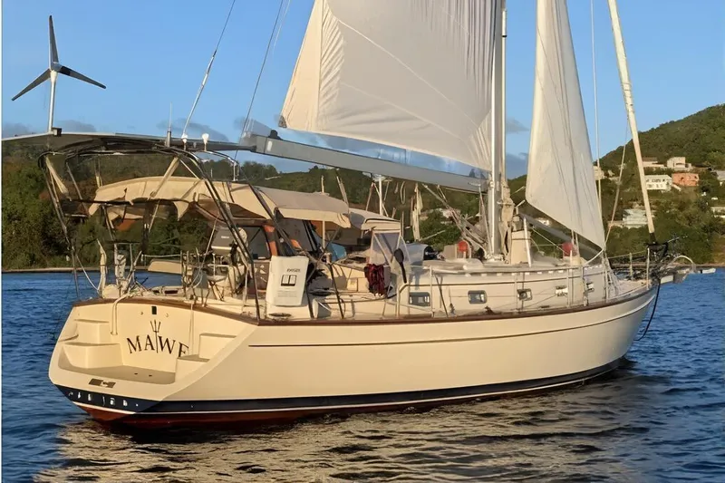 The Image of Island Packet 440 sailboat from 2006 on calm water, featuring white sails and a wind turbine. - 0