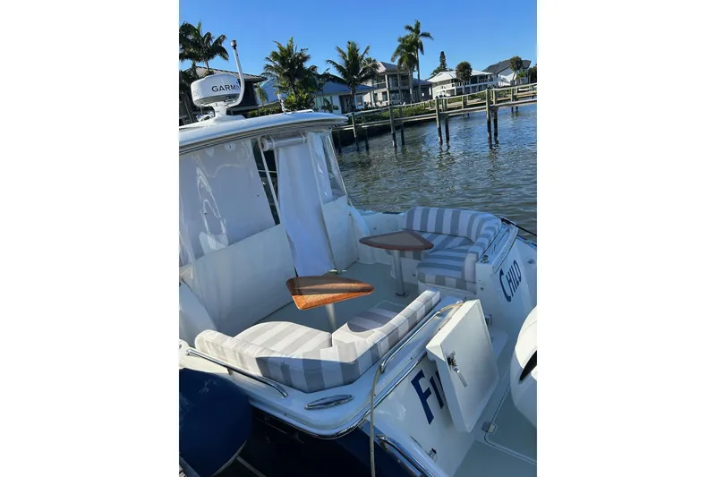 Slide: The Image of 2019 Back Cove 34O boat with striped seating and wooden tables, docked by palm trees. - 6