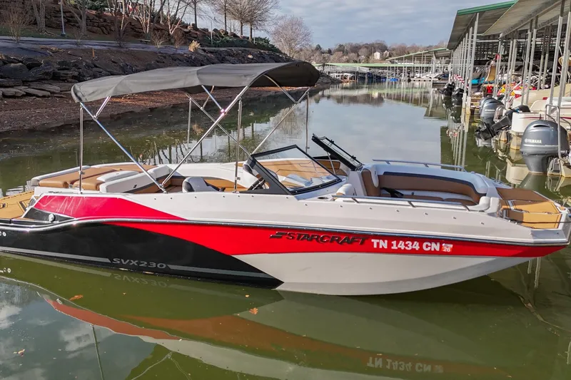 Slide: The Image of 2023 Starcraft SVX 230 IO boat docked on a calm lake with a canopy. - 4