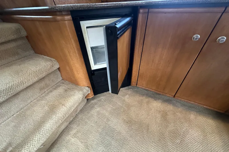 Slide: The Image of 1999 Bayliner 4788 Pilot House Motoryacht interior with open mini fridge and carpeted stairs. - 17