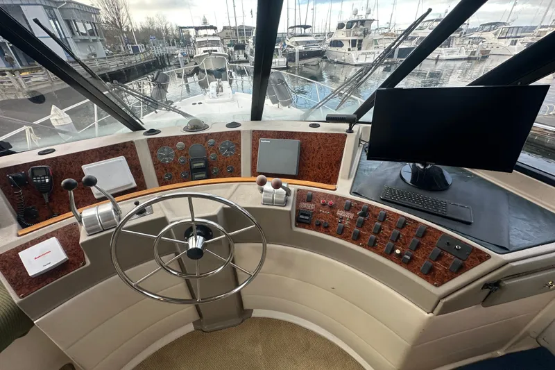 Slide: The Image of 1999 Bayliner 4788 Pilot House Motoryacht helm with steering wheel, controls, and marina view. - 25