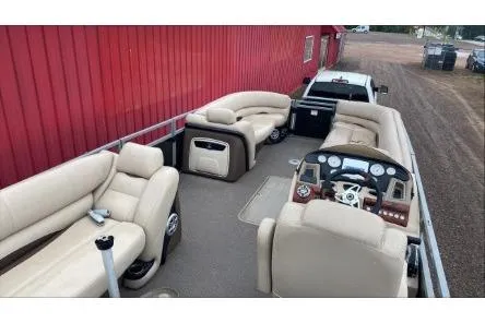 Slide: The Image of 2016 Regency 220 DL3 pontoon boat with beige seating and control panel, parked near a red building. - 4
