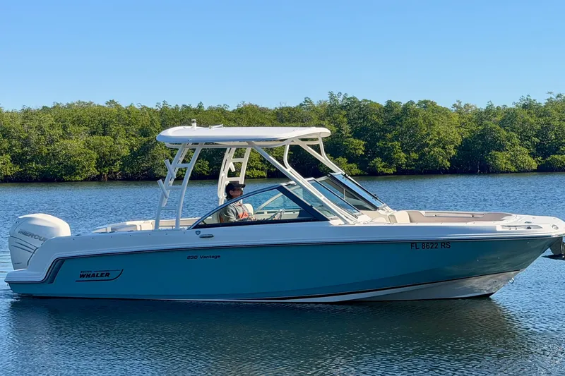 Slide: The Image of 2018 Boston Whaler 230 Vantage boat cruising on a calm lake with lush greenery. - 2