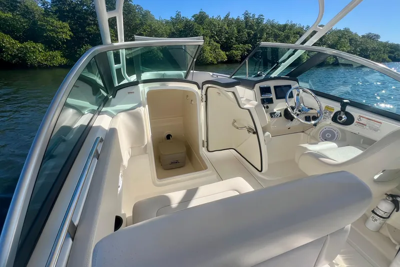 Slide: The Image of 2018 Boston Whaler 230 Vantage boat interior with open storage and steering wheel, near water. - 6