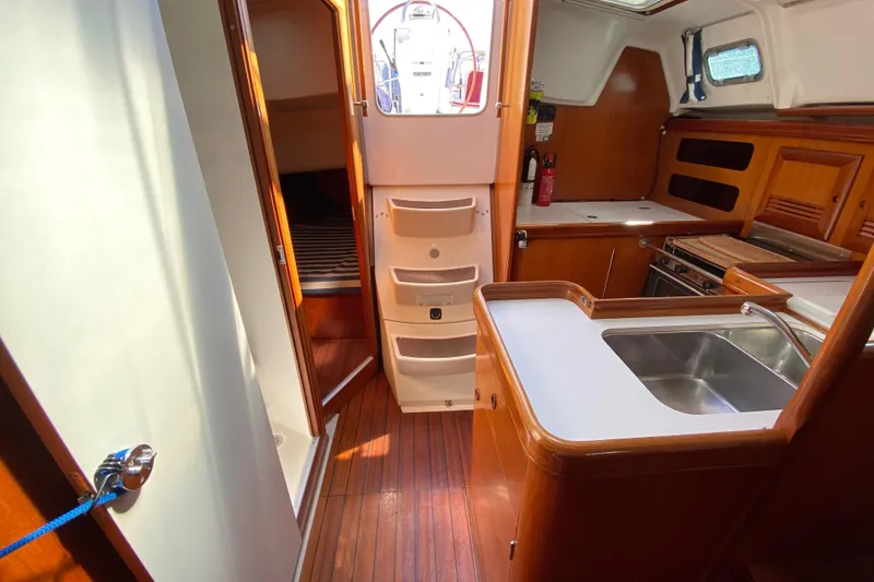 Slide: The Image of Interior of 2001 Beneteau Oceanis 361 sailboat, featuring a compact kitchen and wooden cabinetry. - 64
