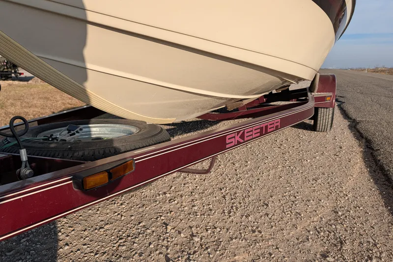 Slide: The Image of 2009 Skeeter SL1900 boat on a red trailer, parked on a gravel road. - 12