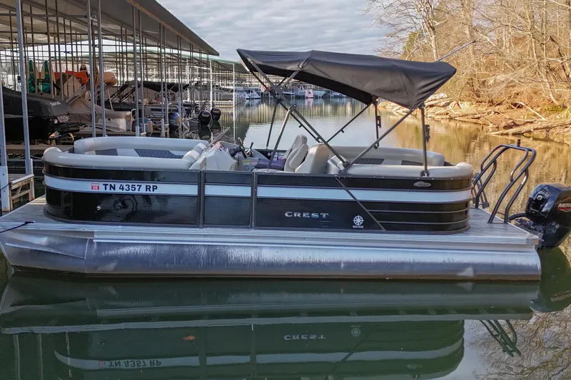 Slide: The Image of 2021 Crest Classic DLX 220 L pontoon boat docked on calm water. - 2