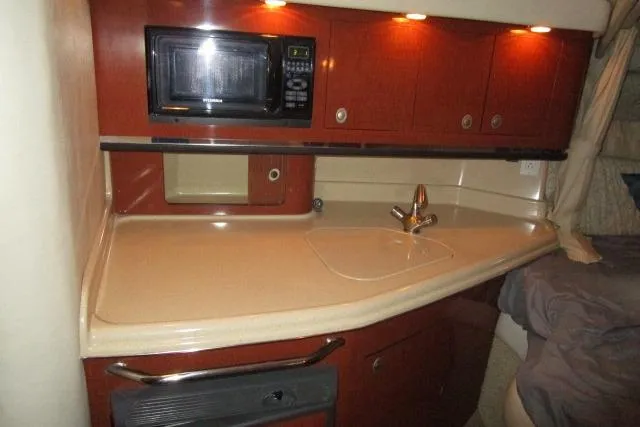 Slide: The Image of 2005 Sea Ray 290 Amberjack interior kitchen with microwave, sink, and wooden cabinets. - 14