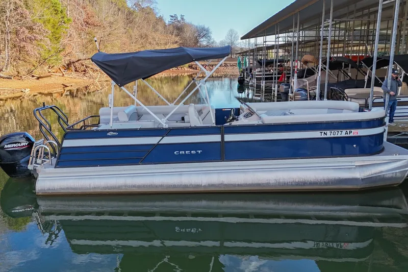 Slide: The Image of 2022 Crest Classic DLX 220 pontoon boat docked on a calm lake. - 2