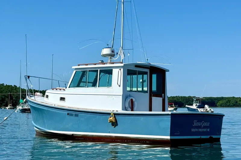 Slide: The Image of 1985 Cape Dory 28 Power Yacht on calm water, blue hull, clear sky background. - 2