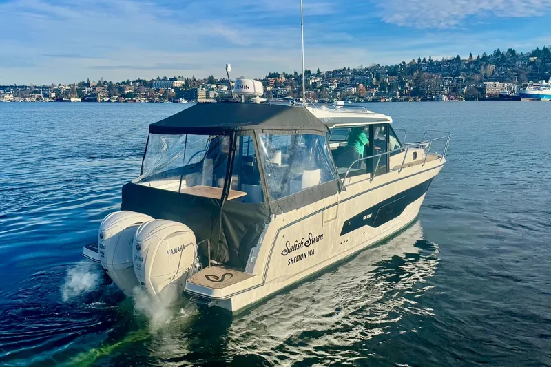Slide: The Image of 2024 Jeanneau NC 1095 Coupe Series 2 cruising on a scenic lake with city backdrop. - 5