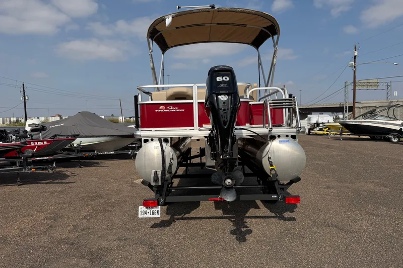 Slide: The Image of 2025 Sun Tracker Bass Buggy 18 DLX pontoon boat with 60 HP engine, parked outdoors. - 90