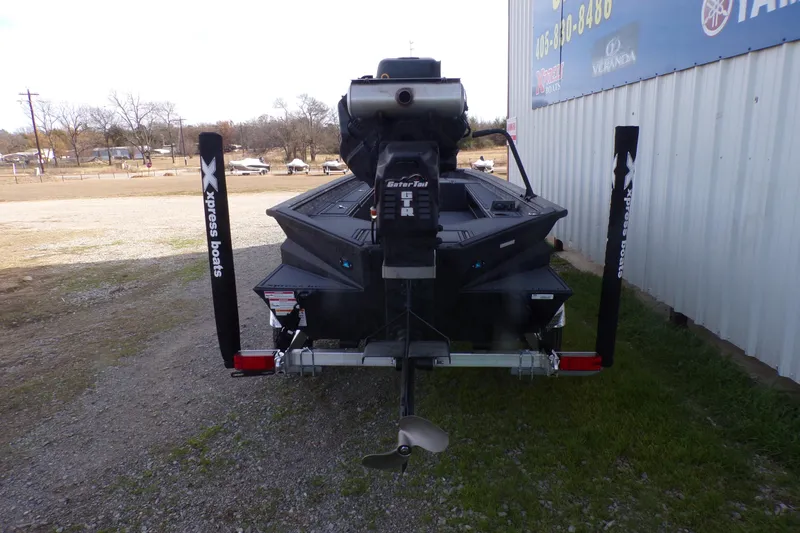 Slide: The Image of 2026 Xpress Bayou 180 boat on trailer, rear view near metal building. - 11