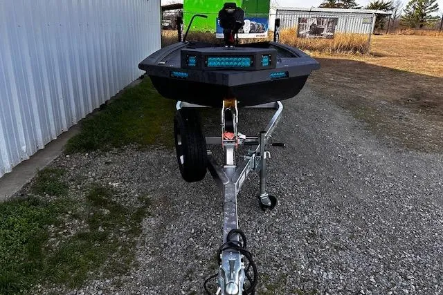 Slide: The Image of 2026 Xpress Bayou 180 boat on trailer, parked on gravel near metal building. - 2