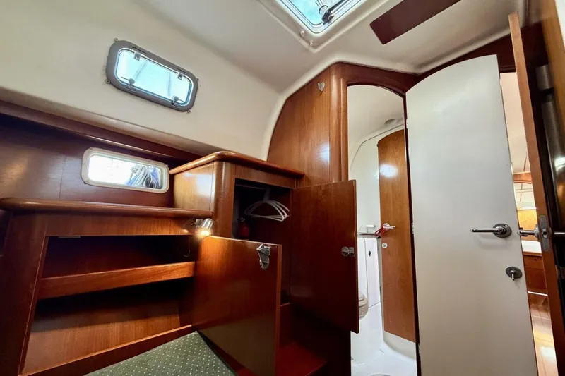 Slide: The Image of Interior of 2000 Beneteau Oceanis 461 yacht, featuring wooden cabinetry and open door to bathroom. - 32
