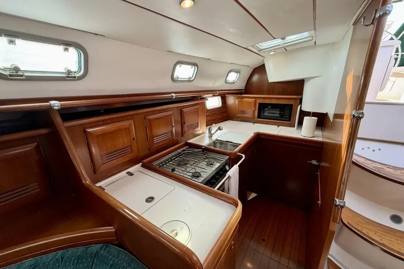 Slide: The Image of Interior of 2000 Beneteau Oceanis 461 yacht, featuring a compact kitchen with wood cabinetry. - 35