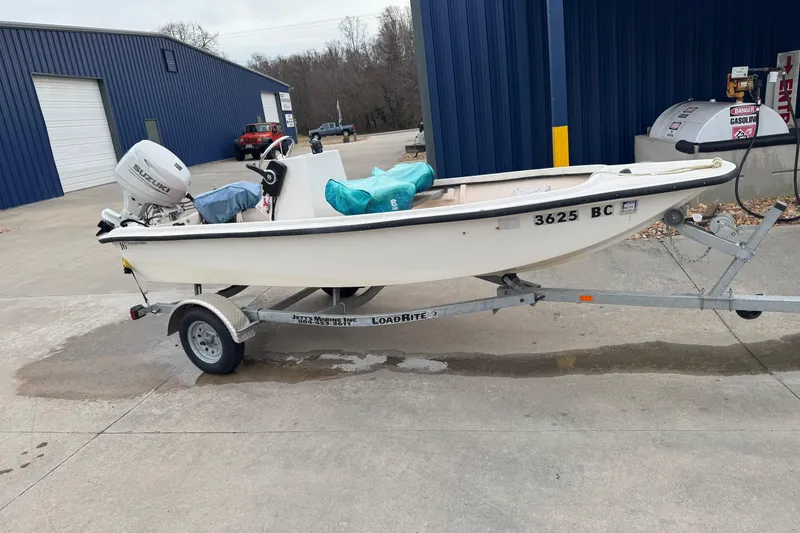 Slide: The Image of 1994 Chincoteague 16 boat on trailer with Suzuki outboard motor, parked near blue building. - 5