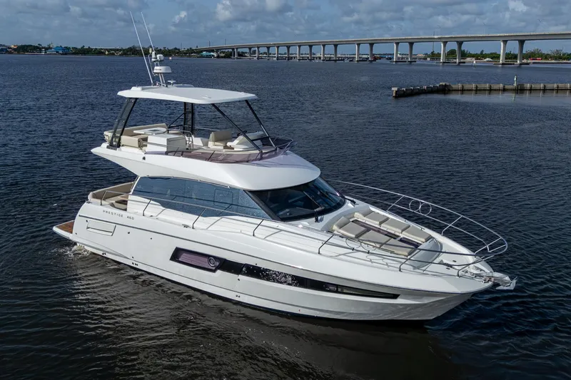 Slide: The Image of 2019 Prestige 460 yacht cruising on a calm river with a bridge in the background. - 3