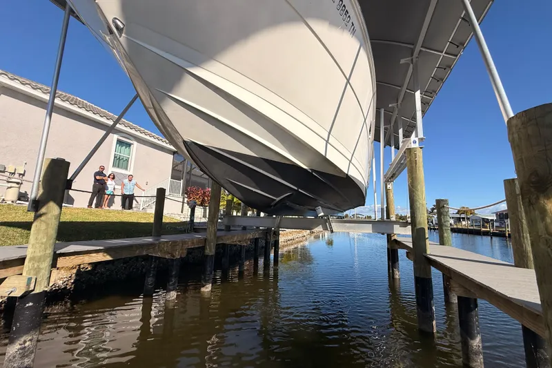 Slide: The Image of 2012 Sea Ray 310 Sundancer boat on lift, dockside view with people in background. - 18