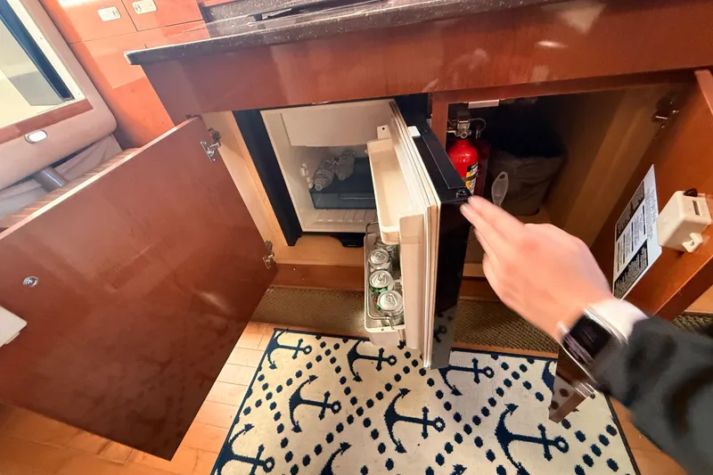 Slide: The Image of Interior of 2012 Sea Ray 310 Sundancer with open mini fridge and nautical-themed rug. - 69