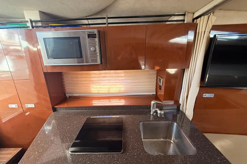 Slide: The Image of Interior of 2012 Sea Ray 310 Sundancer with kitchen, microwave, sink, and wooden cabinetry. - 73