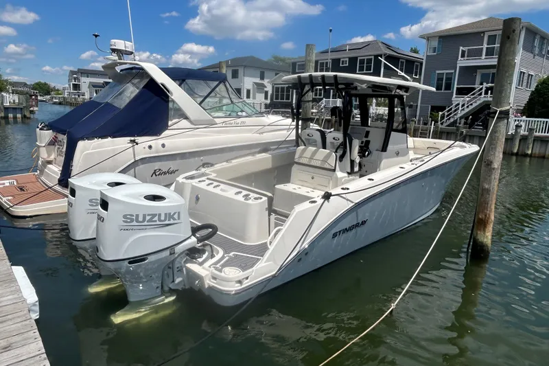 The Image of 2024 Stingray 273 CC boat docked with Suzuki outboard engines, sunny day, waterfront homes. - 0