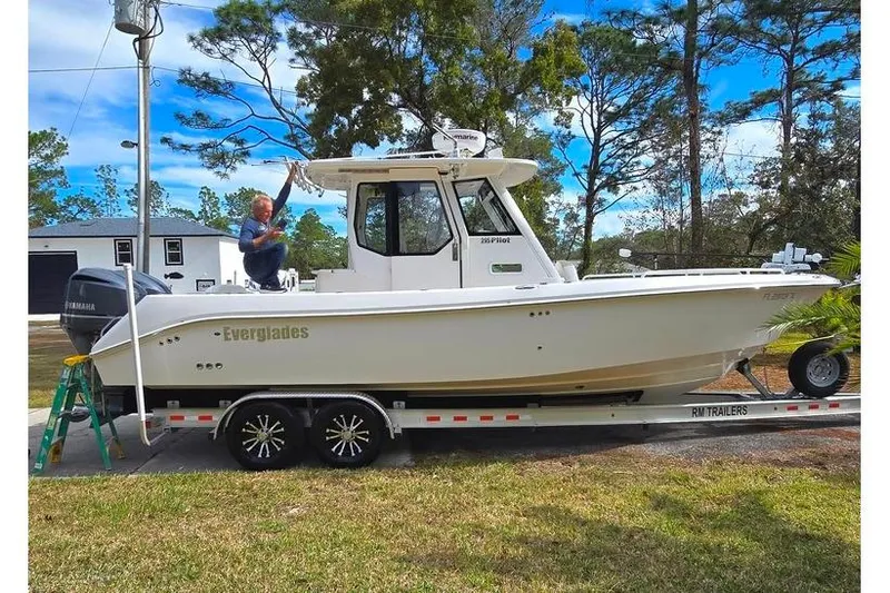 Slide: The Image of 2014 Everglades 295 Pilot boat on trailer, parked outdoors with trees in background. - 2