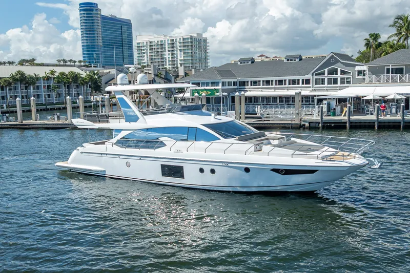 The Image of 2019 Azimut 66 yacht docked in a marina with modern buildings in the background. - 0