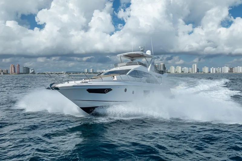 Slide: The Image of 2019 Azimut 66 yacht cruising on open water with city skyline backdrop. - 13