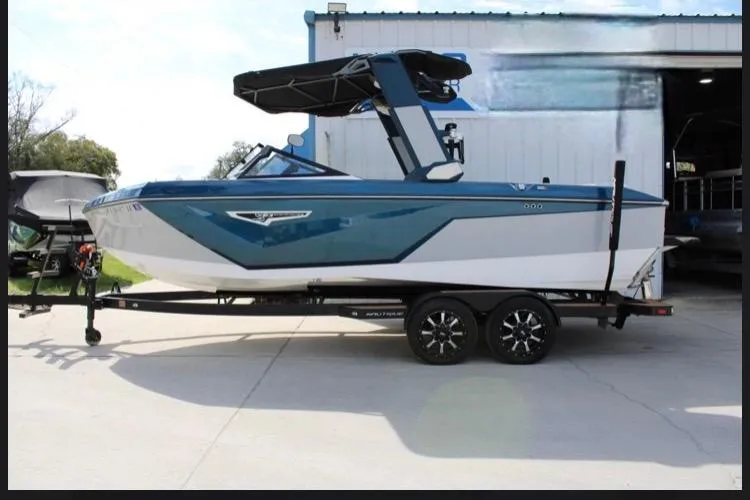 Slide: The Image of 2022 Nautique Super Air Nautique S23 boat on trailer, blue and white design, parked outdoors. - 18
