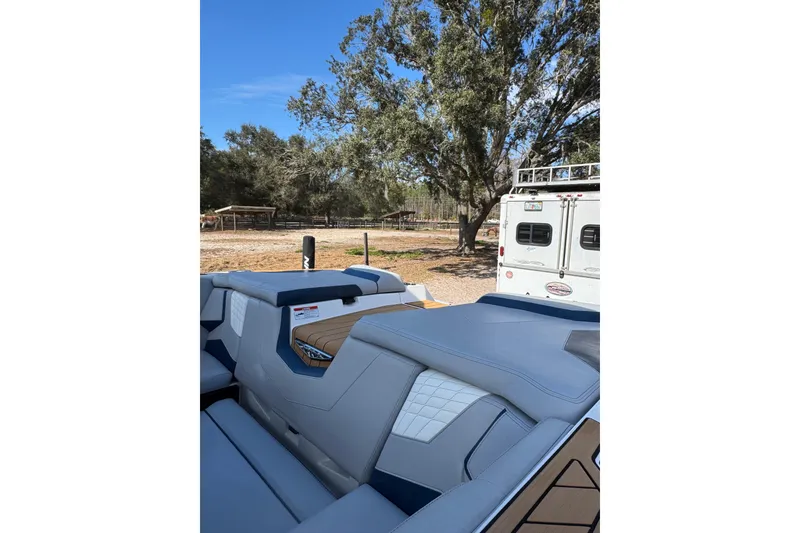 Slide: The Image of 2022 Nautique Super Air Nautique S23 boat interior with blue upholstery, parked outdoors. - 27