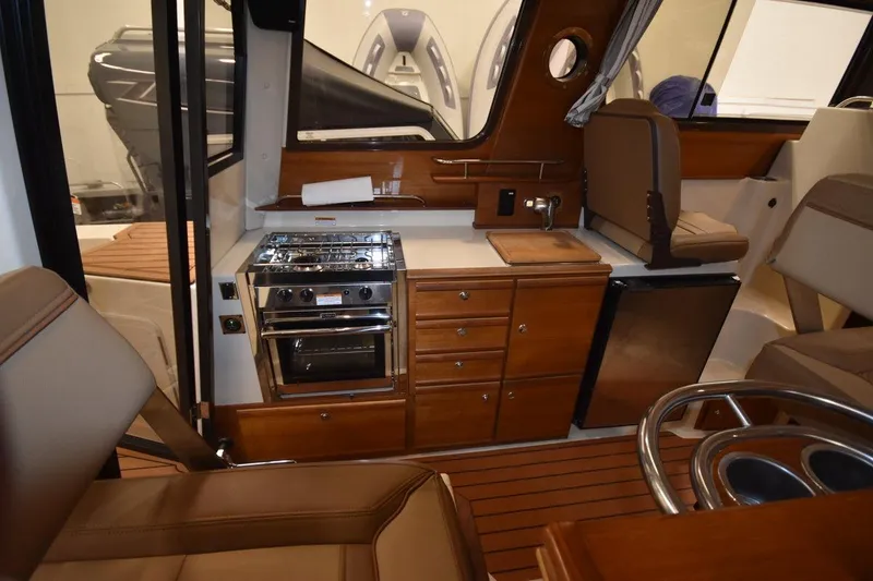 Slide: The Image of 2022 Ranger Tugs R-27 interior with kitchen, stove, fridge, and seating area. - 16