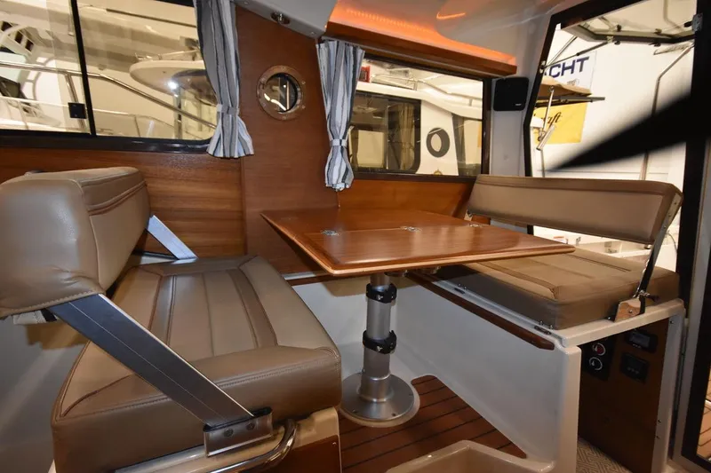 Slide: The Image of 2022 Ranger Tugs R-27 interior with wood table, cushioned seating, and porthole window. - 18