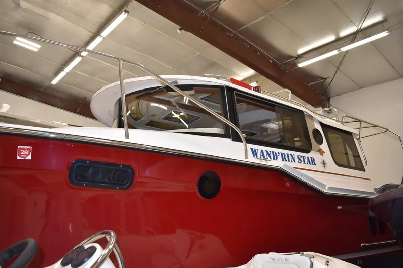 Slide: The Image of 2022 Ranger Tugs R-27 boat, red hull, named "Wand'rin Star," in indoor storage. - 2