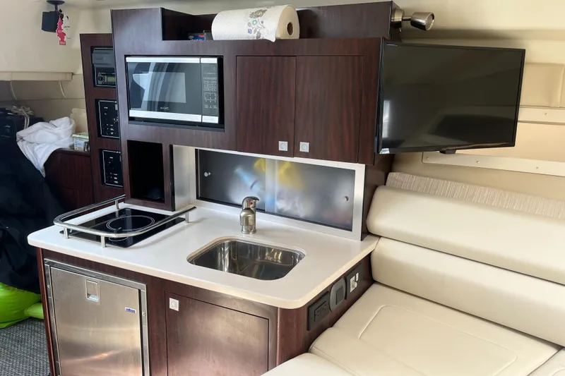 Slide: The Image of 2016 Monterey 295 Sport Yacht interior with kitchenette, microwave, sink, and TV. - 13