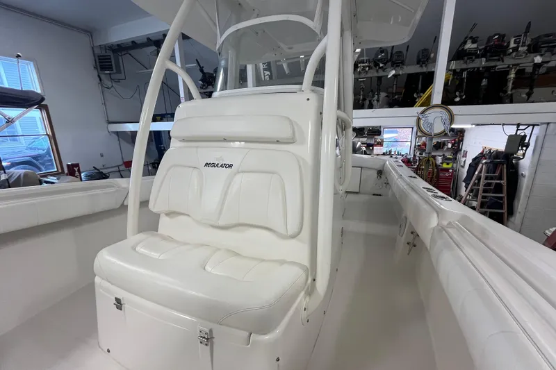 Slide: The Image of 2015 Regulator 25 boat interior with white seating and console in a garage setting. - 54