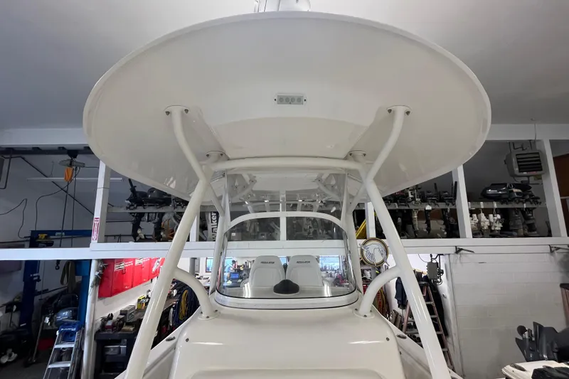 Slide: The Image of 2015 Regulator 25 boat in a garage, showcasing its helm and T-top structure. - 55