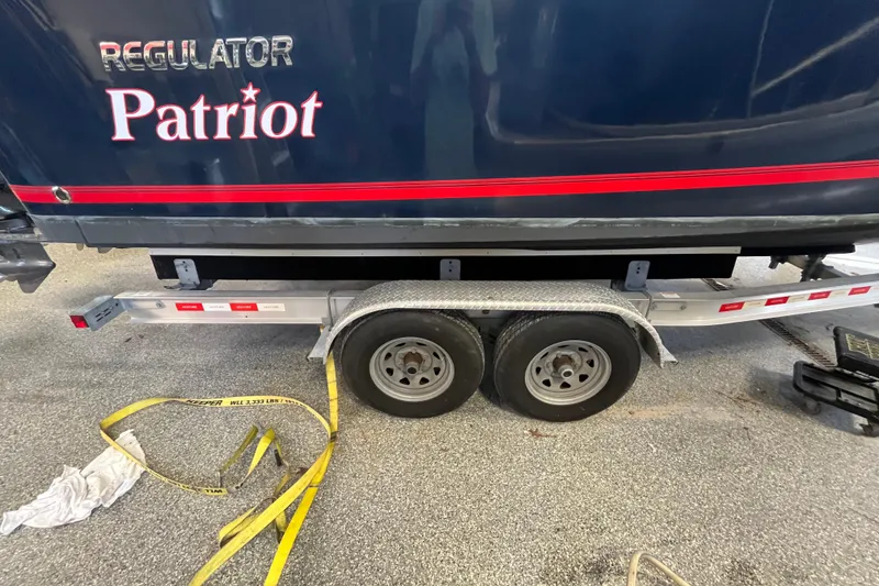 Slide: The Image of 2015 Regulator 25 Patriot boat on trailer, featuring dual wheels and safety straps. - 57