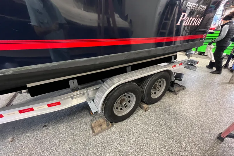 Slide: The Image of 2015 Regulator 25 boat on trailer, featuring dual wheels and red stripe design. - 62
