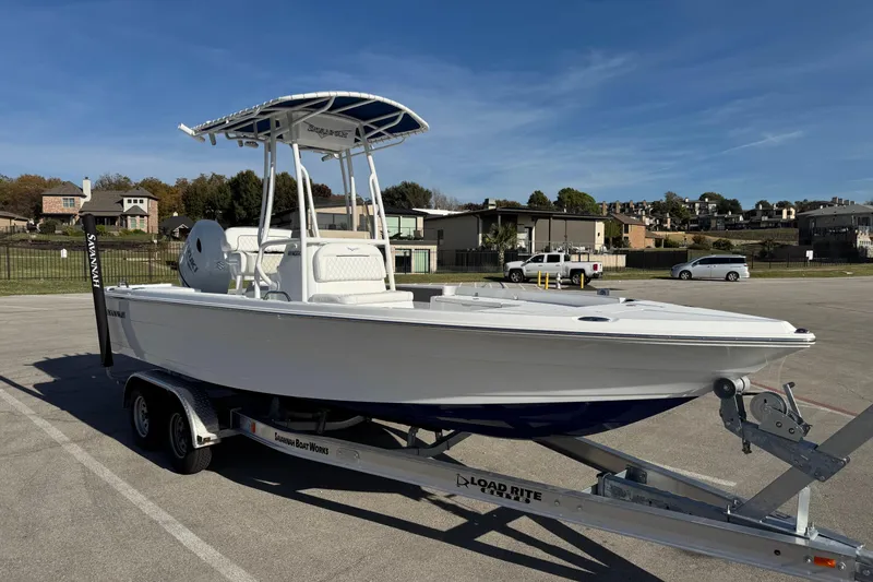 Slide: The Image of 2025 Savannah 210X boat on trailer, parked in a lot with houses in the background. - 2