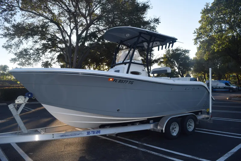 Slide: The Image of 2022 Cobia 220 Center Console boat on trailer in parking lot, surrounded by trees. - 12