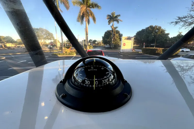 Slide: The Image of Compass on 2022 Cobia 220 Center Console boat, parked near palm trees and parking lot. - 22