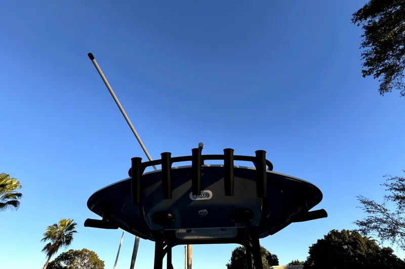 Slide: The Image of 2022 Cobia 220 Center Console boat against clear blue sky, featuring rod holders. - 37