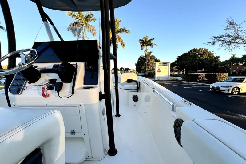 Slide: The Image of 2022 Cobia 220 Center Console boat with steering wheel, parked near palm trees and cars. - 47