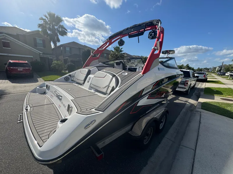 Slide: The Image of 2018 Yamaha Boats 212X on trailer, parked in suburban neighborhood under clear sky. - 14