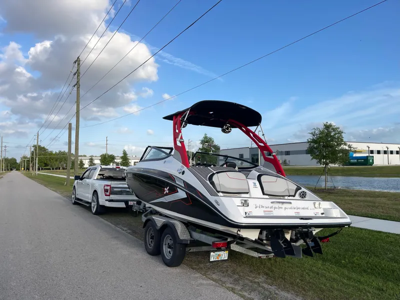 Slide: The Image of 2018 Yamaha Boats 212X on trailer, parked roadside, clear sky, white truck towing. - 4