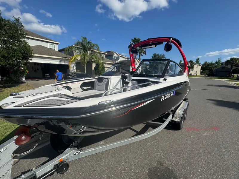 Slide: The Image of 2018 Yamaha Boats 212X on trailer, parked in suburban neighborhood under clear blue sky. - 6