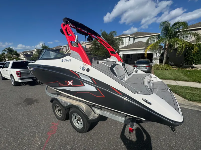Slide: The Image of 2018 Yamaha Boats 212X on trailer, parked in residential area under clear sky. - 8