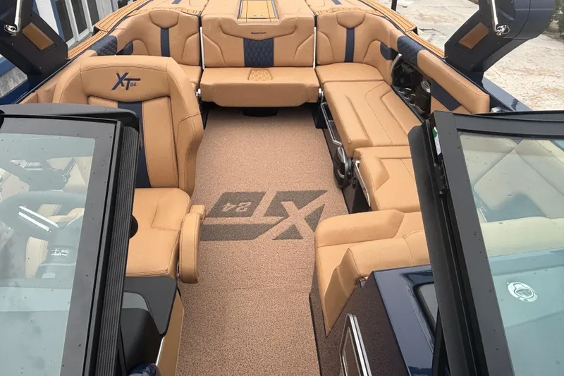 Slide: The Image of 2026 MasterCraft XT24 boat interior with tan seating and logo on carpet. - 6