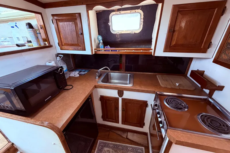 Slide: The Image of 1978 Mainship 34 Trawler kitchen with microwave, stove, sink, and wooden cabinets. - 41